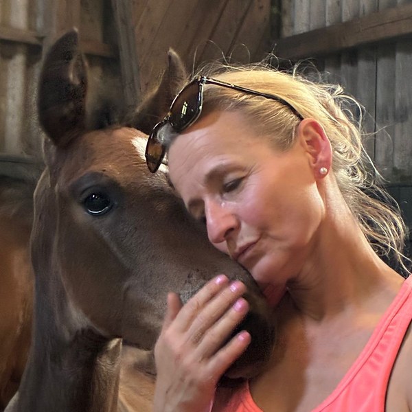 Kati Exner-Zmolek resting her head against a young horse in a barn.